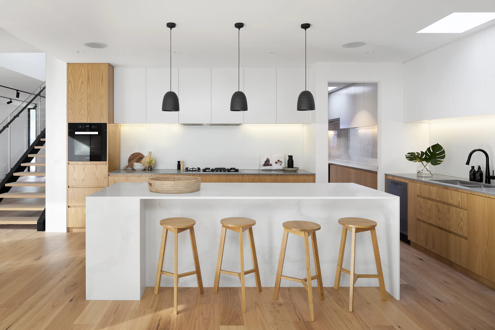Cocina de Casa Tolosa con isla de cuarcita blanca, taburetes de roble y lámparas negras